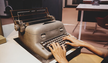 Woman hands type on an old vintage typewriter on the desk in retro room style. Antique typing...