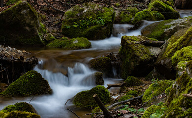 Small waterfall in the forest stream with green moss.
