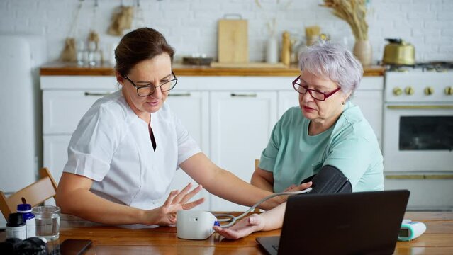 Healthcare worker taking blood pressure of senior woman at home