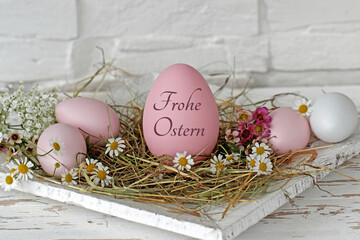 Obraz na płótnie Canvas Frohe Ostern: Kamillenblüten mit Ostereiern in einem Nest. Das Osterei ist mit 