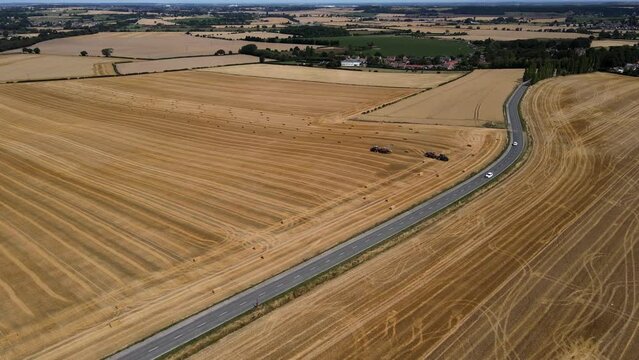 Low flight over cultivated fields with haystacks after harvesting and tractor makes haystacks in Yorkshire region in UK. Aerial motion view