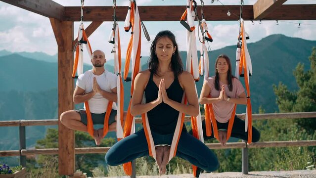 Students meditating in aerial yoga hammocks outdoors