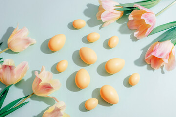 Yellow Easter eggs and tulip flowers on green background in sunlight. Easter concept. Top view, flat lay