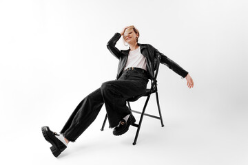 A carefree young woman lounges in a chair, dressed in trendy black attire against a white background