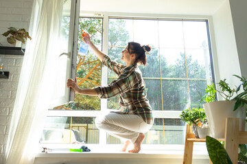 Woman manually washes the window of the house with a rag with spray cleaner and mop inside the...