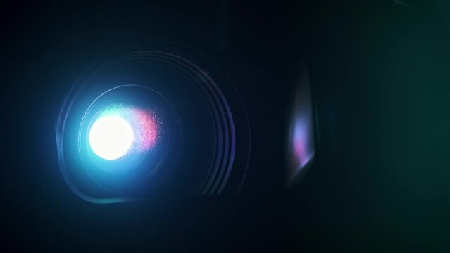Multi-colored projector emits bright beams for broadcasting movies. Close-up view of lens flare, light transitions, prism effects on black background. Ideal for home theater or business presentations