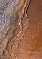 Ocean surf on sandy beach, top view. Nature background with red sand and waved lines of seawater on a sand shoreline. - 748985346