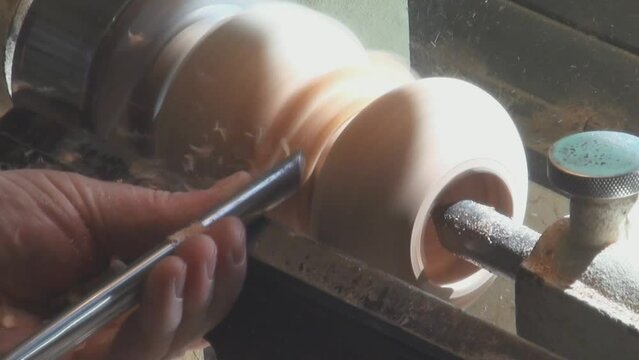 A turner makes a wooden vase on a lathe