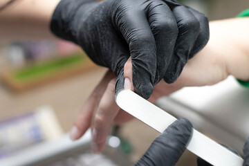 Beauty concept. A manicurist in black latex gloves makes a hygienic manicure, paints the client's...