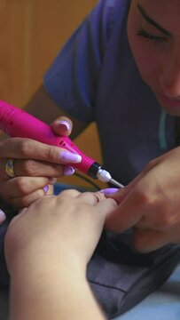 Latin nail artist woman using manicure electrical torno or polisher machine on acrylic nails of unrecognizable client 