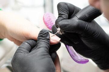 Beauty concept. A manicurist in black latex gloves makes a hygienic hardware manicure with a Fraser...