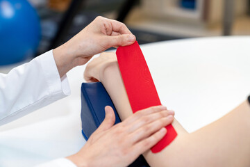 Physical therapist placing kinesio tape on patient's elbow. Therapy with kinesio tex tape....