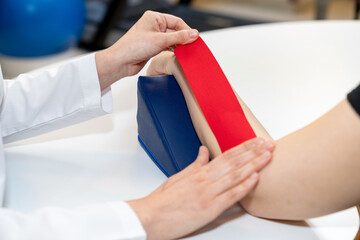 Physical therapist placing kinesio tape on patient's elbow. Therapy with kinesio tex tape. Therapeutic treatment of elbow with kinesio tape. kinesio treatment after sports muscle injury.  - obrazy, fototapety, plakaty