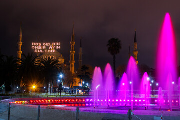 Fototapeta premium Hoş geldin ya şehri Ramazan (Translate: Welcome month of ramadan) lettering hanging on Mosque's mahya. Mahya is an enlightenment arrangement during ramadan nights between two minarets.