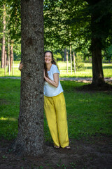 Beautiful woman with gorgeous curly hair hugging tree, dressed in white and yellow combination, hugging the tree, smiling. Concept: active, healthy life, in love with nature, support