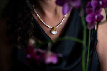Woman in black satin dress with beautiful white necklace. Pearl necklace on a woman neck with a...