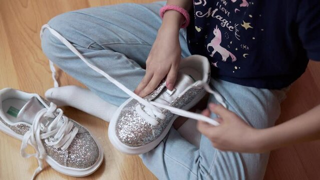 A teenage girl takes off the laces from her sneakers. Silver shiny sneakers with a white sole in the hands of a teenage girl