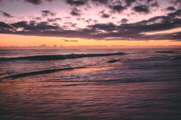 Obraz premium Sunrise on a Florida beach, sea foam on shore, clouds above the horizon