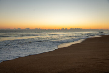 Sunrise on a Florida beach, sea foam on shore, clouds above the horizon