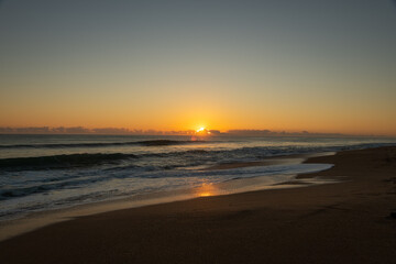 Sunrise on a Florida beach, sea foam on shore, clouds above the horizon