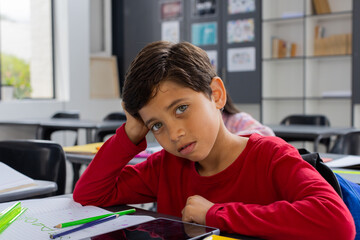 Biracial boy with brown hair looks sad in a school classroom setting