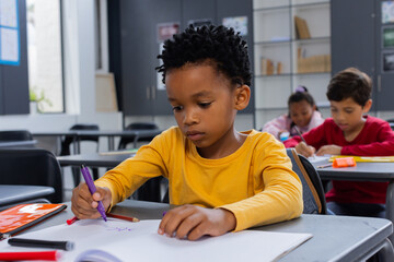 African American boy focused on drawing with a purple marker in a school classroom