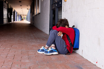 Biracial boy sits alone in school, head resting on knees, looking distressed