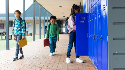 Biracial boy and African American boy walk past a biracial girl at school lockers