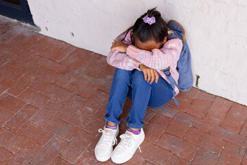 Biracial girl appears upset, sitting on the ground with her head down, with copy space