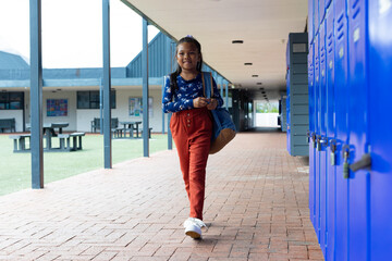 Biracial girl with a backpack stands by blue lockers at school
