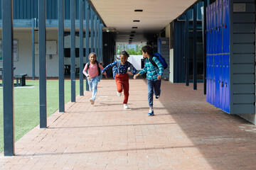 Biracial boy and girl run joyfully with another child through a school corridor with copy space