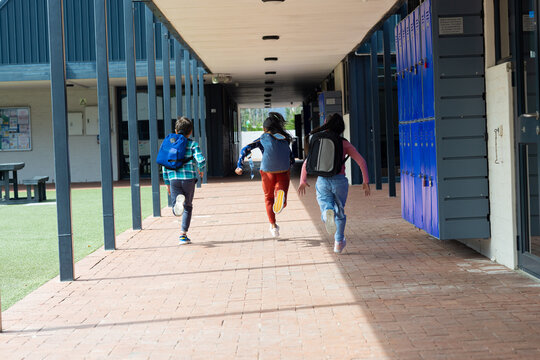 Three children are running through a school corridor with lockers on the right, with copy space