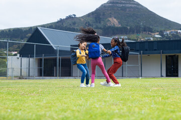 Fototapeta premium Three biracial girls are playing on a grassy field in school, with a mountain in the background