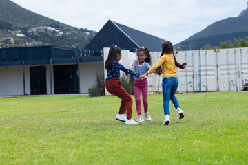 Three girls are playing and holding hands in a grassy outdoor area in school