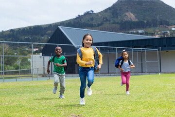 Three children are joyfully running across a grassy field during the day in school