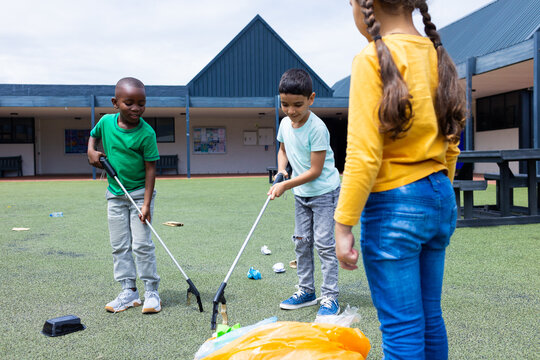 Biracial boy and African American boy are picking up trash, biracial girl watches