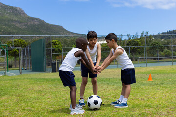 Three boys are huddled over a soccer ball on a grassy field, ready to play in school