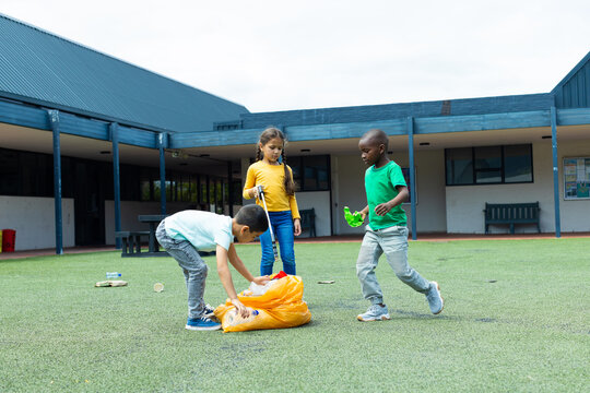 Biracial girl in a yellow top observes as a biracial boy picks up litter