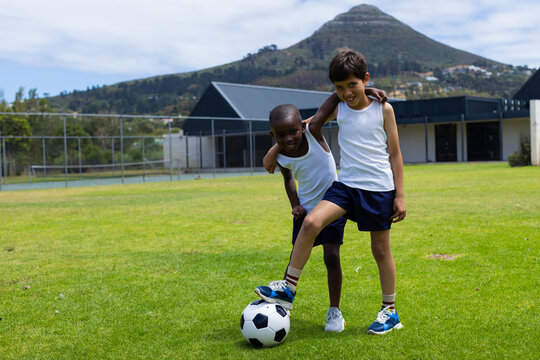 Biracial boy and African American boy play soccer outdoors in school with copy space