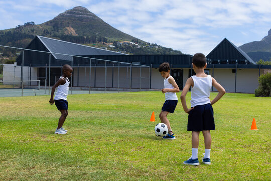 Biracial and African American boys play soccer outdoors at school, with mountains in the background