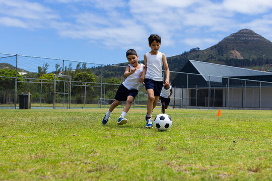 Two boys are playing soccer on a sunny day in school, with one chasing the ball