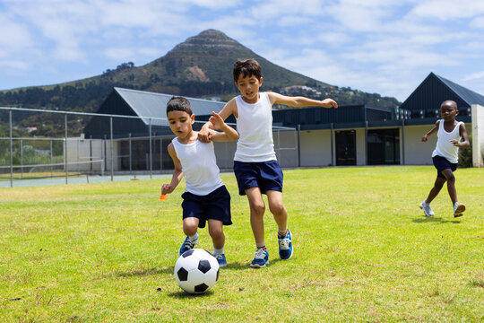 Biracial and African American boys play soccer outdoors at school, with a mountain in the background