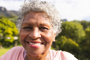 Senior biracial woman with curly gray hair smiles warmly outdoors