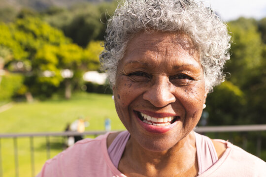 Senior biracial woman with curly gray hair smiles warmly outdoors