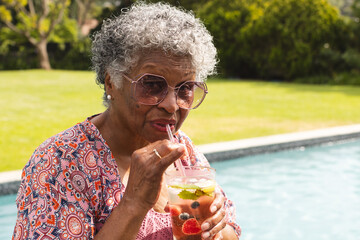 Senior biracial woman sips a drink by the pool
