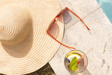 A straw hat, sunglasses, and a refreshing drink sit under the sunlight with copy space