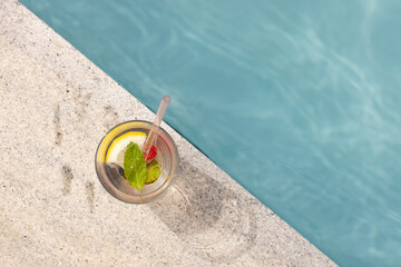 A refreshing drink with lemon and mint sits by a poolside with copy space