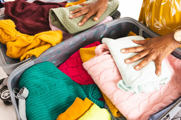 Hands pack colorful clothes into an open suitcase, suggesting travel preparation