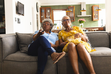 Senior African American woman and senior biracial woman sit together on a couch, watching TV