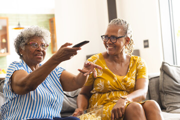 Senior African American woman points at the TV with a remote, as her companion smiles at home